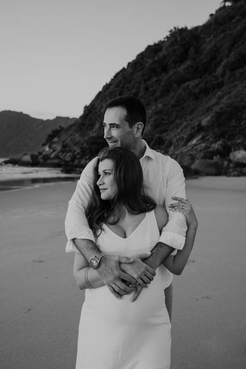 Foto em preto e branco do casal abraçado em momento de conexão na praia.'