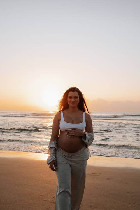 Foto da gestante de frente destacando a barriga com o sol brilhando atrás.'
