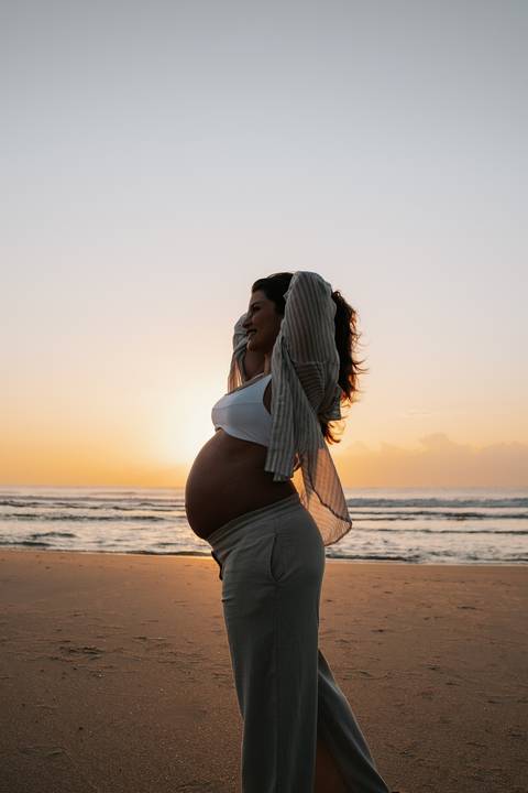Foto de perfil da gestante em estilo silhueta com céu em tons de laranja.'