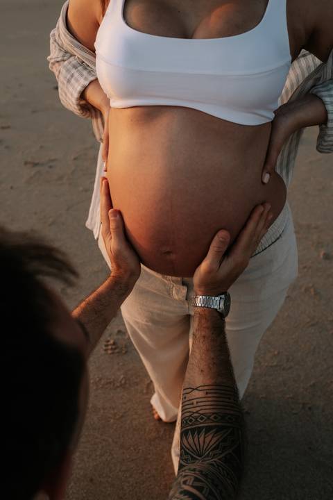 Foto em detalhe das mãos do parceiro segurando a barriga da gestante.'