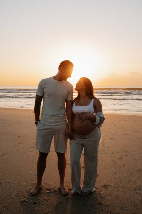Foto do casal em pé na areia com o sol brilhando entre os dois.'