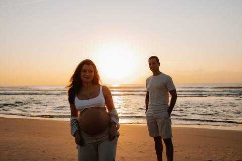 Foto da silhueta do casal em pé na praia com luz solar intensa ao fundo.'