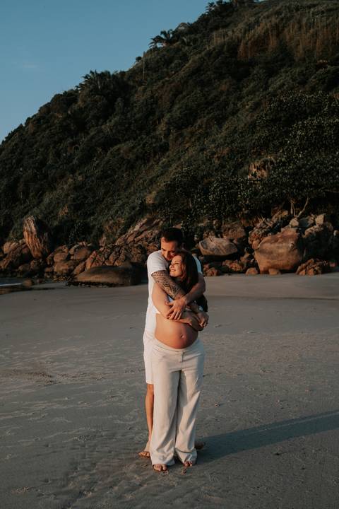 Foto do casal abraçado na beira da praia em momento de acolhimento.'