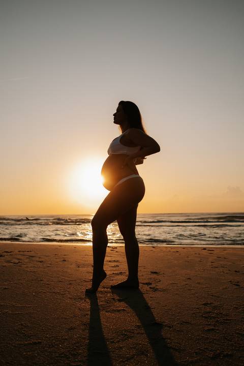 Foto de silhueta da gestante de perfil com o sol iluminando a barriga.'