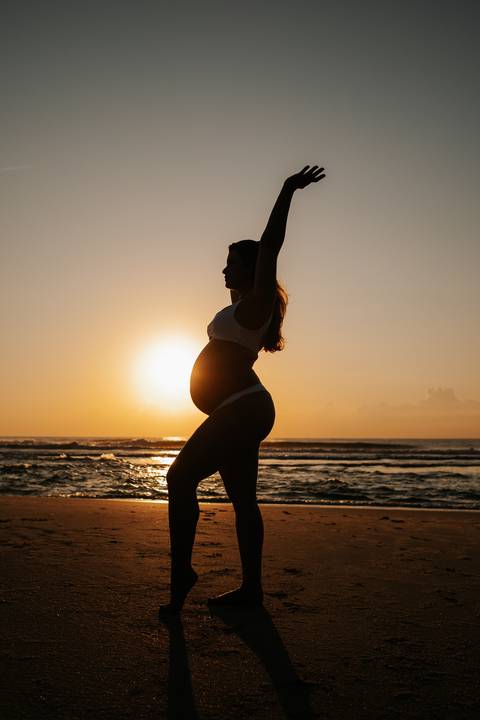 Foto da silhueta da gestante de perfil com o sol alinhado à barriga no amanhecer.'
