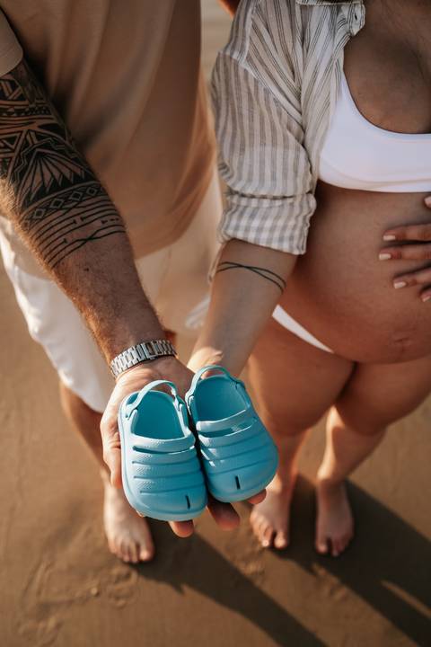 Foto aproximada do casal exibindo os sapatinhos azuis em frente à barriga.'