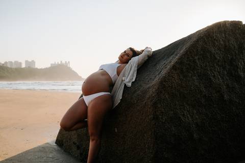 Foto da gestante deitada em uma rocha destacando a silhueta da gravidez.'