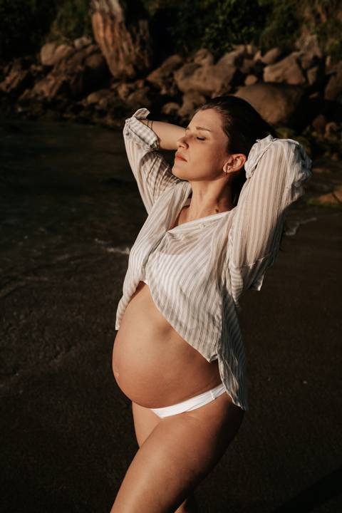 Foto da gestante de camisa branca aberta destacando a barriga.'
