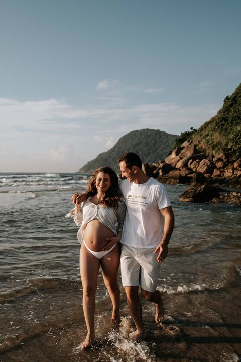 Foto do casal sorrindo na areia molhada no amanhecer.'
