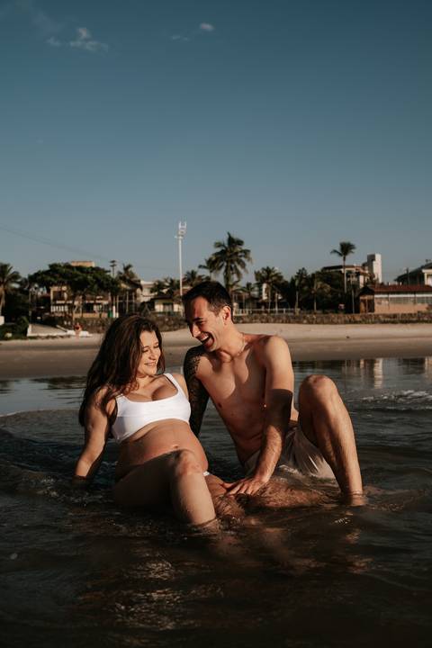 Foto do casal rindo e se divertindo na beira do mar.'