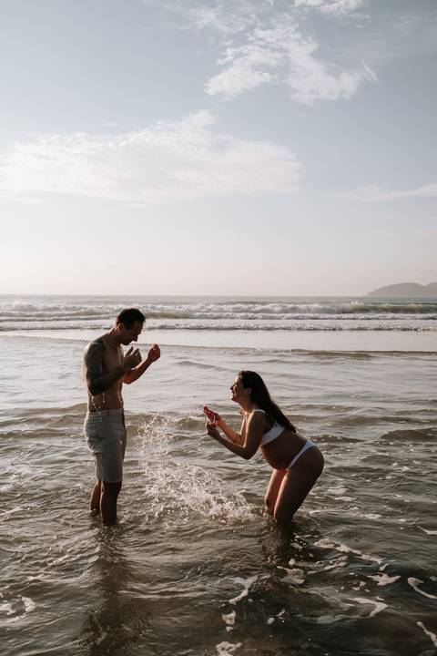 Foto do casal brincando com a água do mar no nascer do sol.'