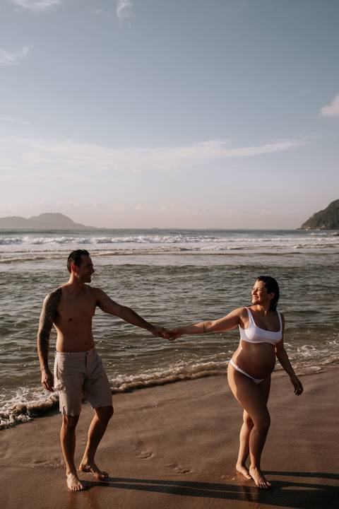 Foto do casal trocando olhares enquanto caminham na beira do mar.'