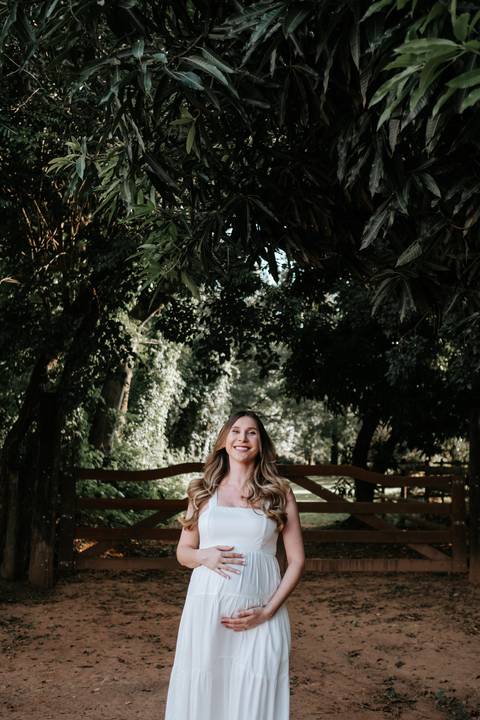 Foto aproximada da gestante sorrindo em meio à vegetação da fazenda.'