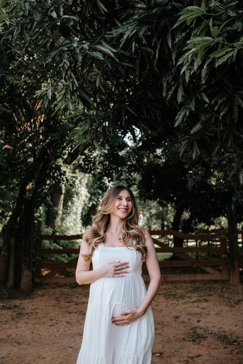 Foto de perfil da gestante sorridente com fundo de natureza.'