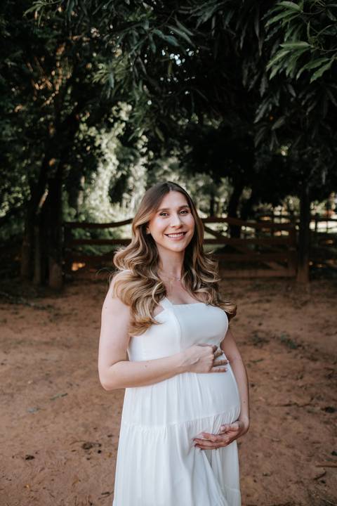 Foto de close da gestante com as mãos na barriga e expressão alegre.'