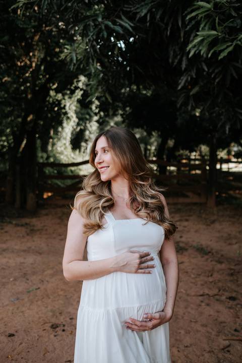 Foto da gestante olhando para o lado em momento espontâneo no campo.'
