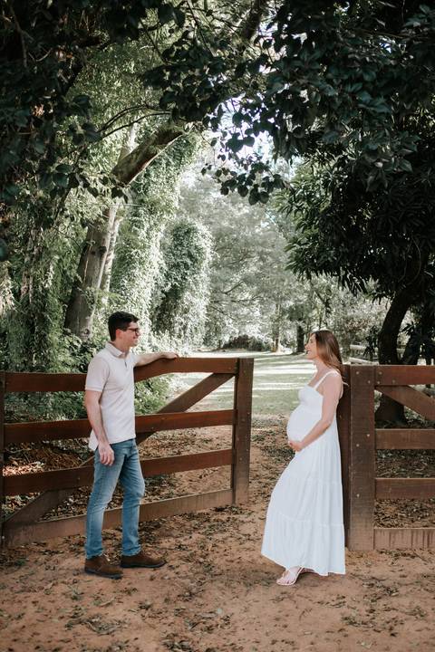 Foto do casal posando em frente à porteira aberta na fazenda.'