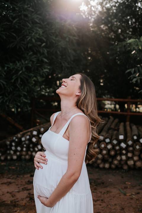 Foto da gestante rindo com o rosto voltado para o céu.'