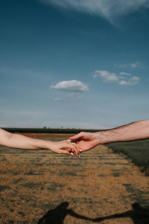 Foto em detalhe das mãos do casal unidas com o horizonte ao fundo.'