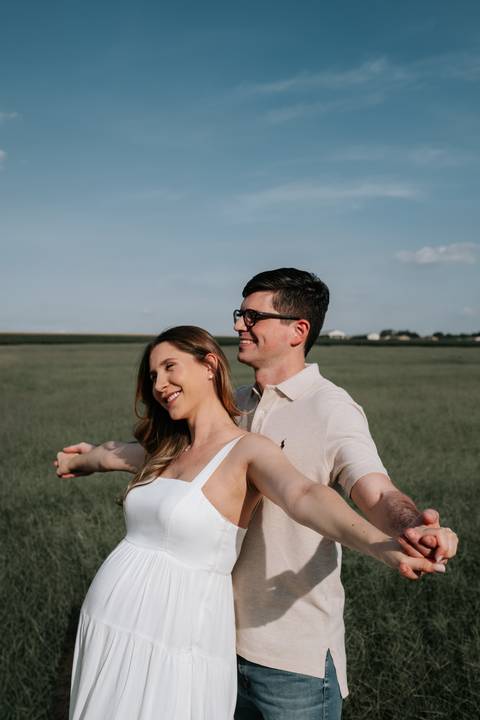 Foto do casal brincando e sorrindo em plano aberto na plantação.'