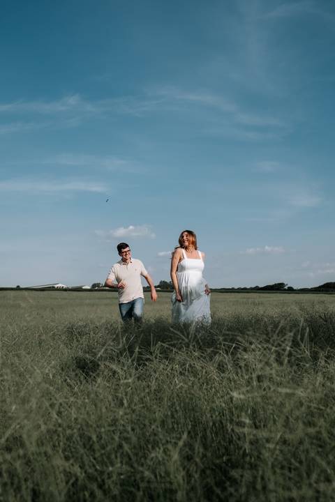 Foto do casal correndo e brincando no campo aberto.'