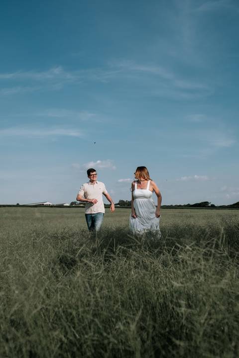 Foto do casal sorrindo e correndo na plantação.'