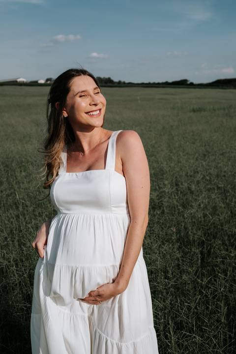 Foto aproximada da gestante destacando a barriga e o sorriso.'