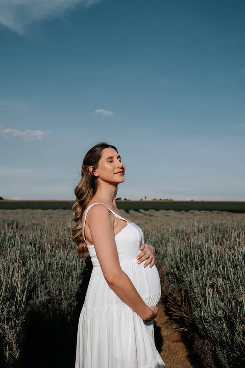 Foto de perfil da gestante de olhos fechados sob o sol.'