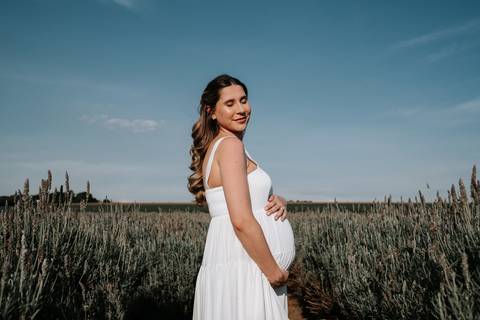 Foto da gestante de perfil segurando a barriga no campo.'