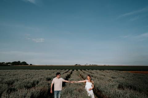 Foto do casal de mãos dadas em plano aberto na plantação.'