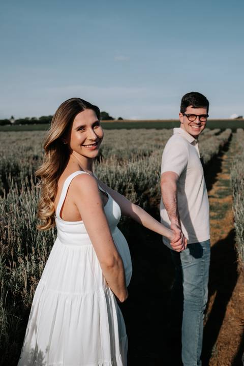 Foto da gestante sorrindo enquanto o parceiro a puxa pela mão.'