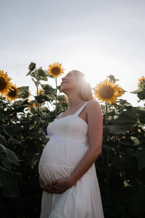 Foto aproximada da gestante com girassóis iluminados pelo sol.'