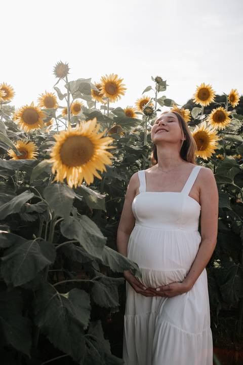 Foto da gestante de olhos fechados com girassóis ao fundo.'