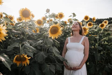 Foto da gestante sorrindo em meio à plantação de girassóis.'