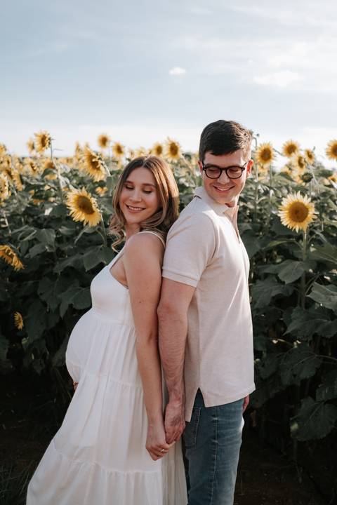 Foto do casal de costas um para o outro sorrindo entre os girassóis.'