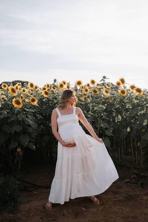 Foto da gestante segurando o vestido branco em momento fluido.'