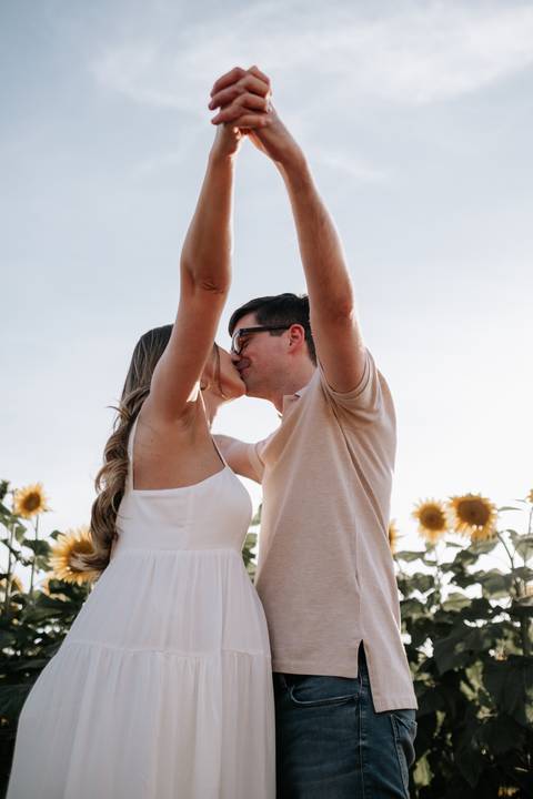 Foto do casal se beijando sob a luz natural do campo.'