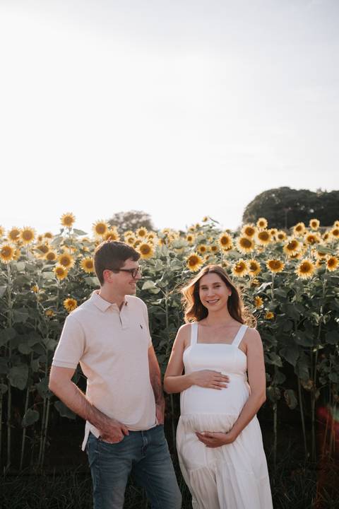 Foto aproximada do casal sorrindo cercado por girassóis.'