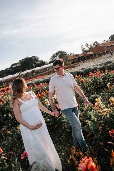 Foto do casal caminhando de mãos dadas pelo campo florido.'