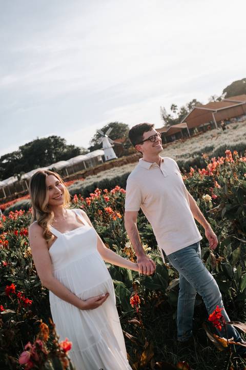 Foto do casal sorrindo e caminhando entre flores coloridas.'