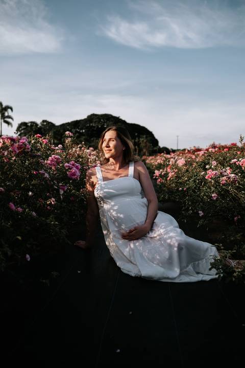 Foto da gestante sentada em meio a flores cor-de-rosa.'