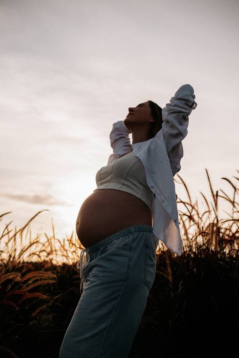 Foto da silhueta da barriga da gestante contra o sol poente.'