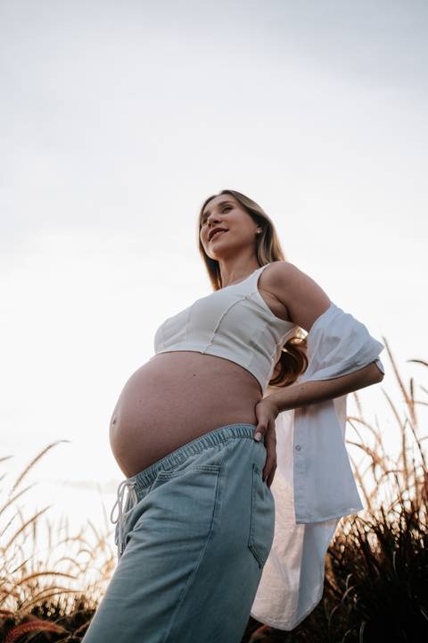 Foto de perfil da gestante destacando a barriga sob luz dourada.'