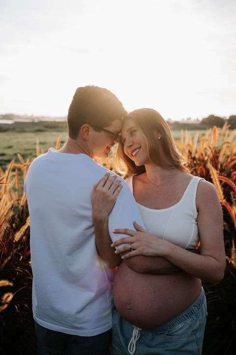 Foto do casal encostando os rostos sob a luz do pôr do sol.'
