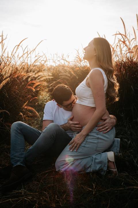Foto do pai beijando a barriga da gestante sob a luz dourada.'