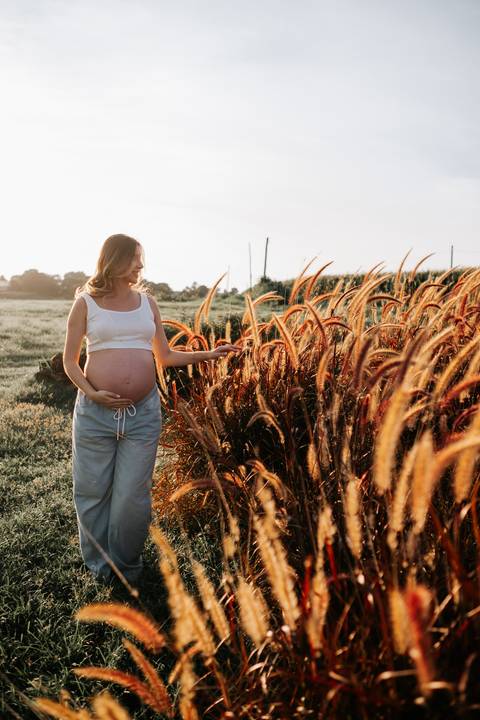 Foto da gestante de perfil caminhando pelo campo iluminado.'