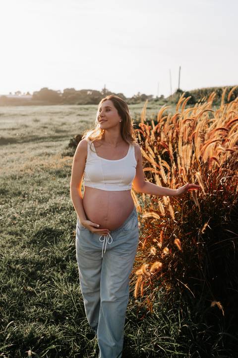 Foto da gestante de frente destacando a barriga no campo.'