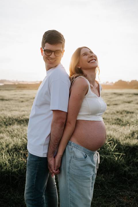 Foto do casal de costas um para o outro sorrindo no pôr do sol.'