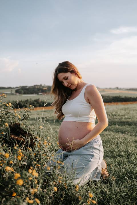 Foto da gestante olhando para a barriga em momento sereno.'