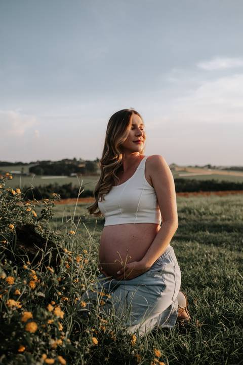 Foto da gestante sorridente com a luz do sol ao fundo.'